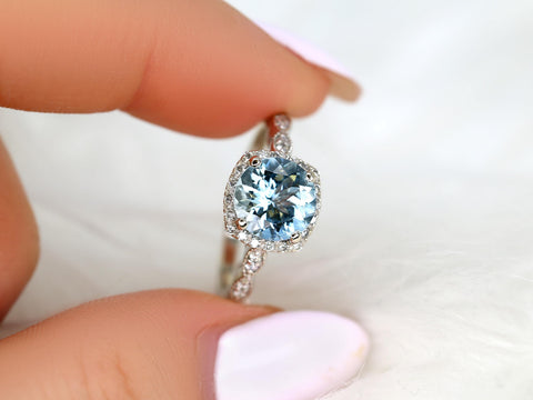 Close-up of a hand holding an 8mm aquamarine center ring with diamond accents and milgrain cushion halo on a delicate band