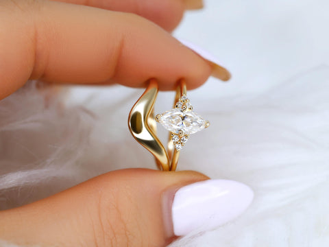 Hand holding a marquise moissanite cluster bridal set with a curved gold wedding band on a soft white background