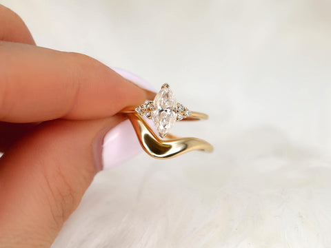 Hand holding 14kt gold bridal set with marquise moissanite cluster engagement ring and curved wedding band on white fabric