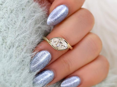 Hand with silver metallic nails wearing a marquise diamond solitaire on a slender gold band, elegant fine jewelry ring.