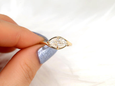 Hand holding a gold band with a horizontally set marquise diamond solitaire ring on a white background
