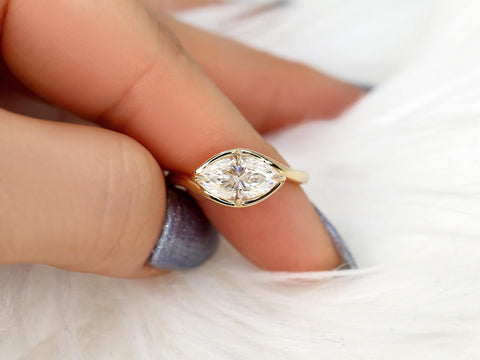 Close-up of a hand holding a marquise diamond solitaire ring set horizontally on a delicate yellow gold band.