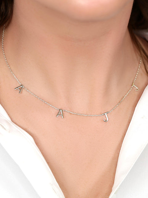 Silver necklace with letter pendants on a person wearing a white top