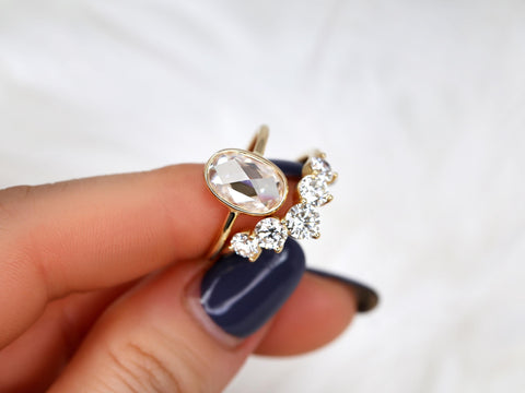 rose cut moissanite oval bezel ring with 5 stone wedding ring pinched between 2 fingers