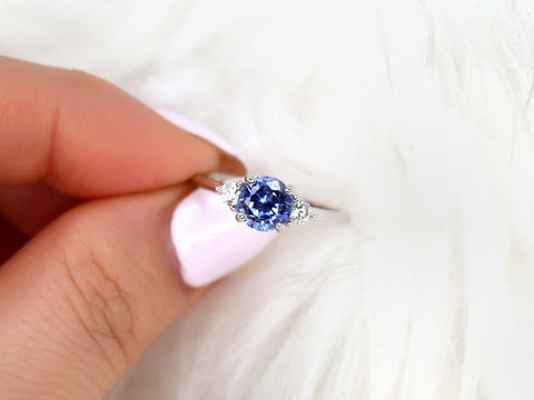 cornflower blue sapphire trilogy ring between finger and white background
