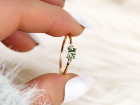 oval green sapphire ring in trilogy with two diamonds on yellow gold presented pinching fingers