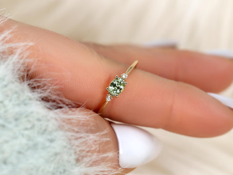 oval green sapphire ring in three stone style with two diamonds on 14kt gold on pointed finger