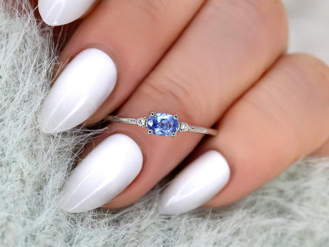 oval cornflower blue sapphire ring in trilogy style with two diamonds on white gold on ring finger