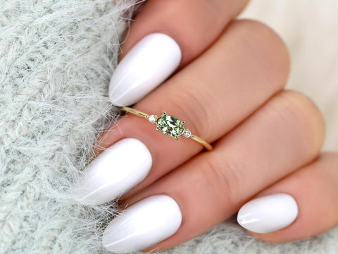 oval green sapphire ring in three stone with two diamonds on yellow gold presented middle finger
